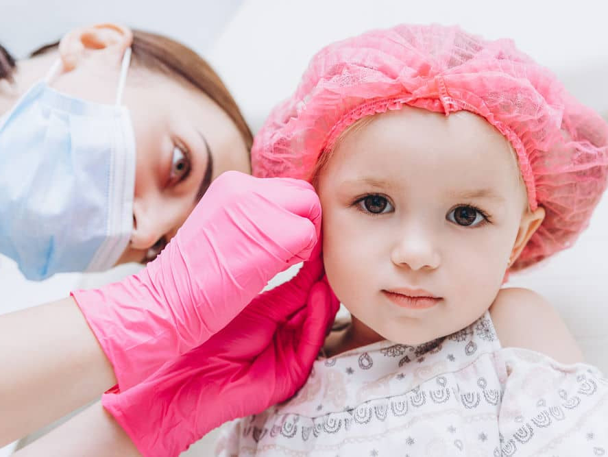 Children's ear piercing: Image by Anna Nass via Shutterstock - Charming little girl having an ear piercing process